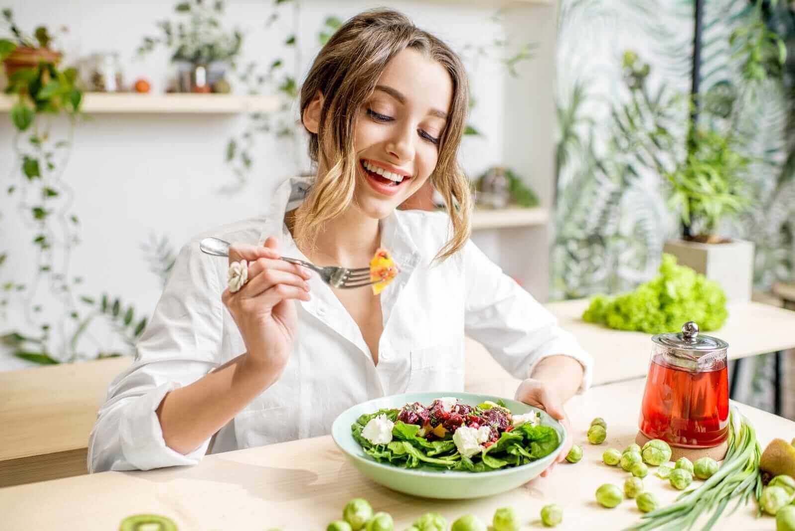 A smiling woman holding a fork and a bowl of salad_ Image by RossHelen via Shutterstock_