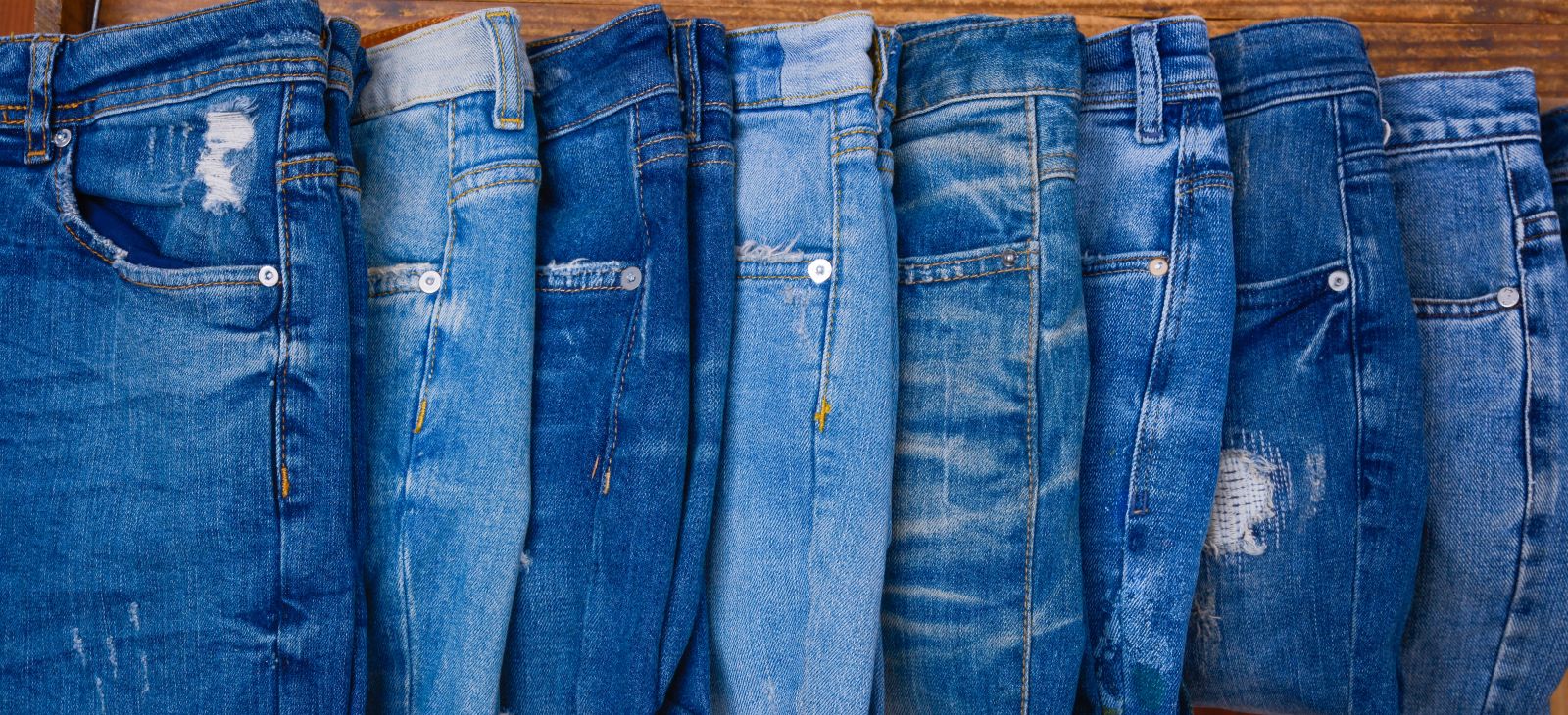 Various blue jeans on wooden background_ Image by Apollofoto via Shutterstock_