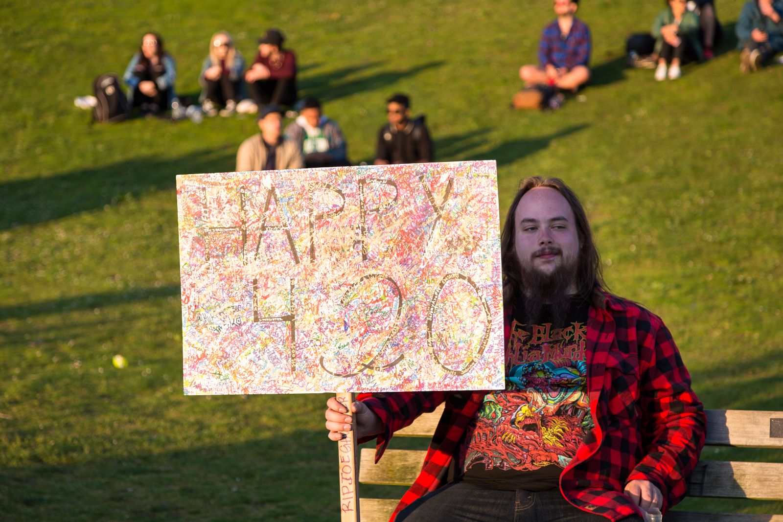 A man holding a sign that says Happy 420 on a grassy hill by Adam Melnyk via Shutterstock