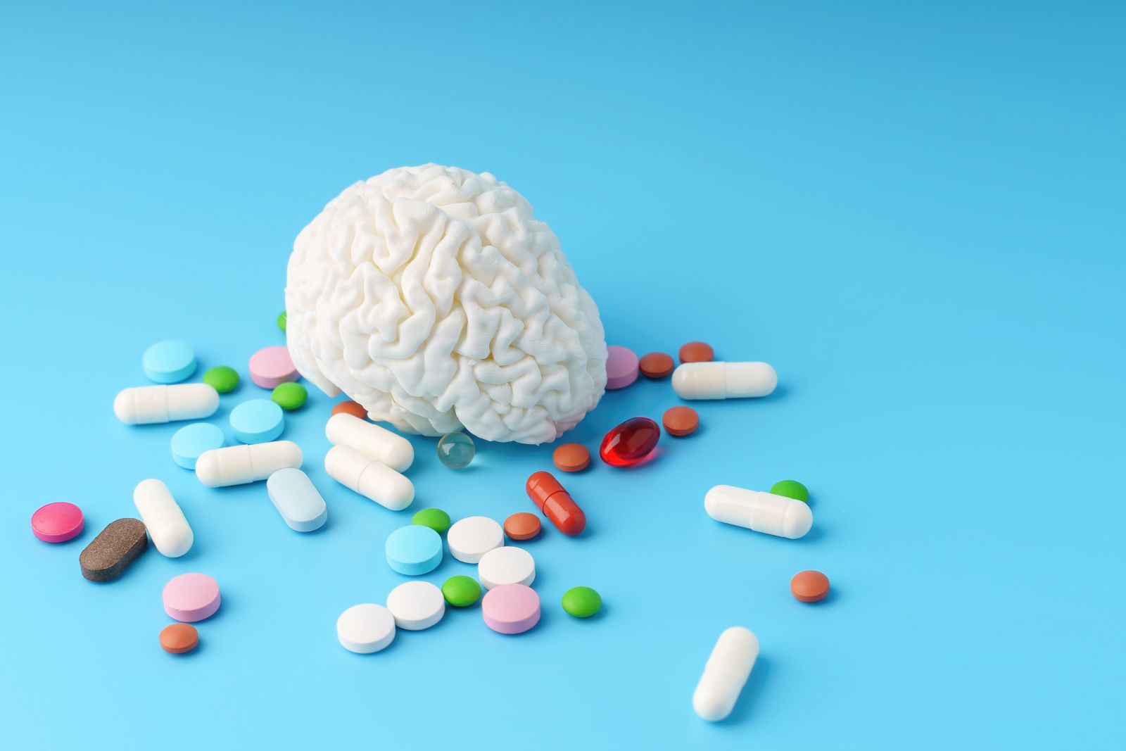 A concept image of a white brain on a blue background surrounded by colorful pills by Tanita_St via Shutterstock