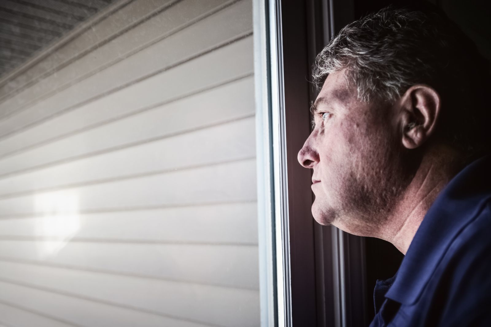 A man in a dark-blue collared shirt looking out the window by Suzanne Tucker via Shutterstock