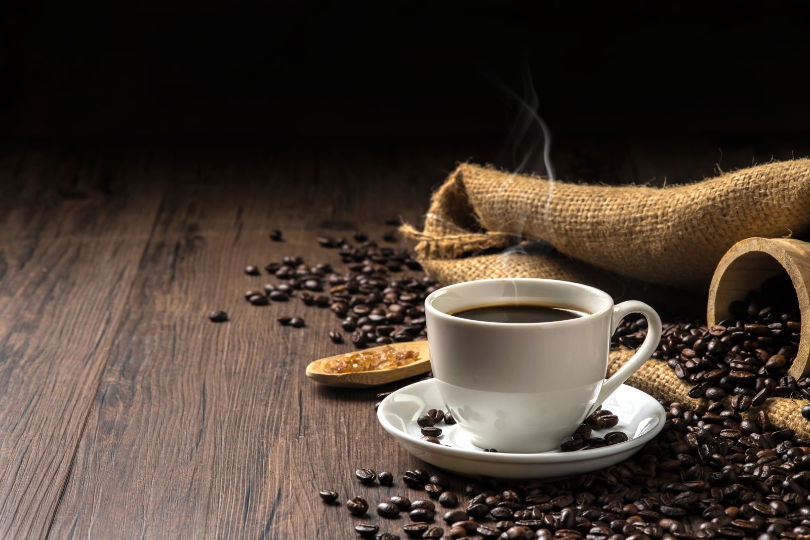 Coffee - Hot coffee in a white coffee cup and many coffee beans by Kingmaya Studio via Shutterstock