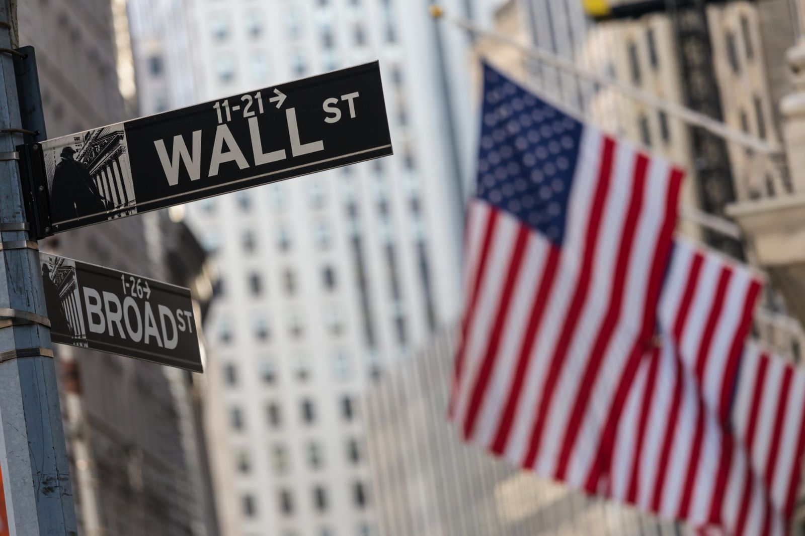 Wall Street - Wall street sign in New York City with American flags and New York Stock Exchange in background by kasto80 via iStock