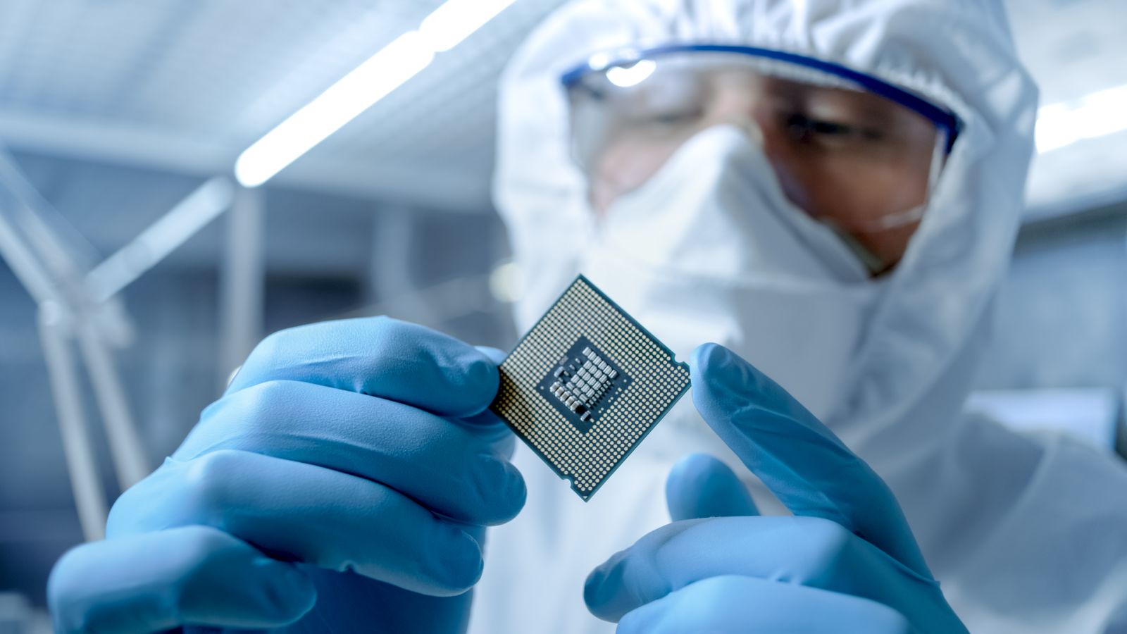 Engineer in Sterile Coverall Holds Microchip with Gloves and Examines it by Gorodenkoff via Shutterstock